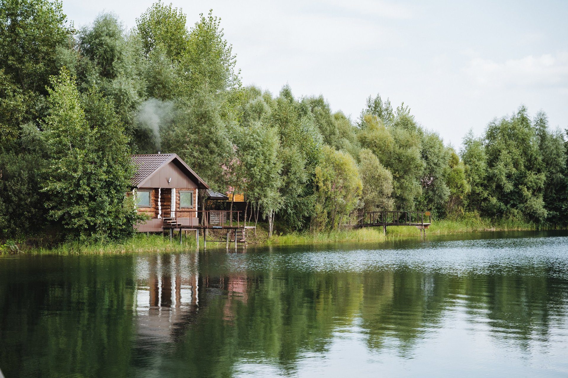 A quaint wooden house peacefully sitting on the edge of a beautiful lake surrounded by tall trees and lush greenery