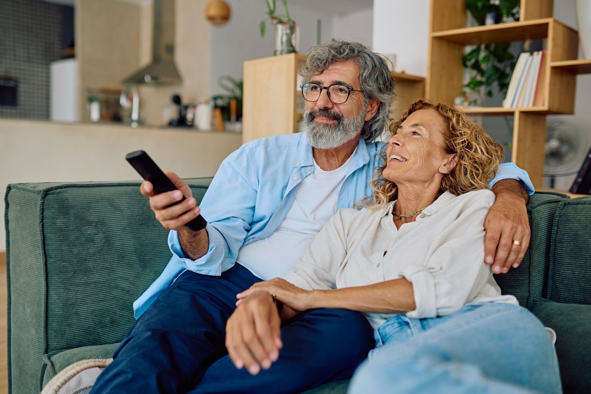 Happy retired couple enjoying quality time together while watching television in their cozy living room, embracing relaxation and connection