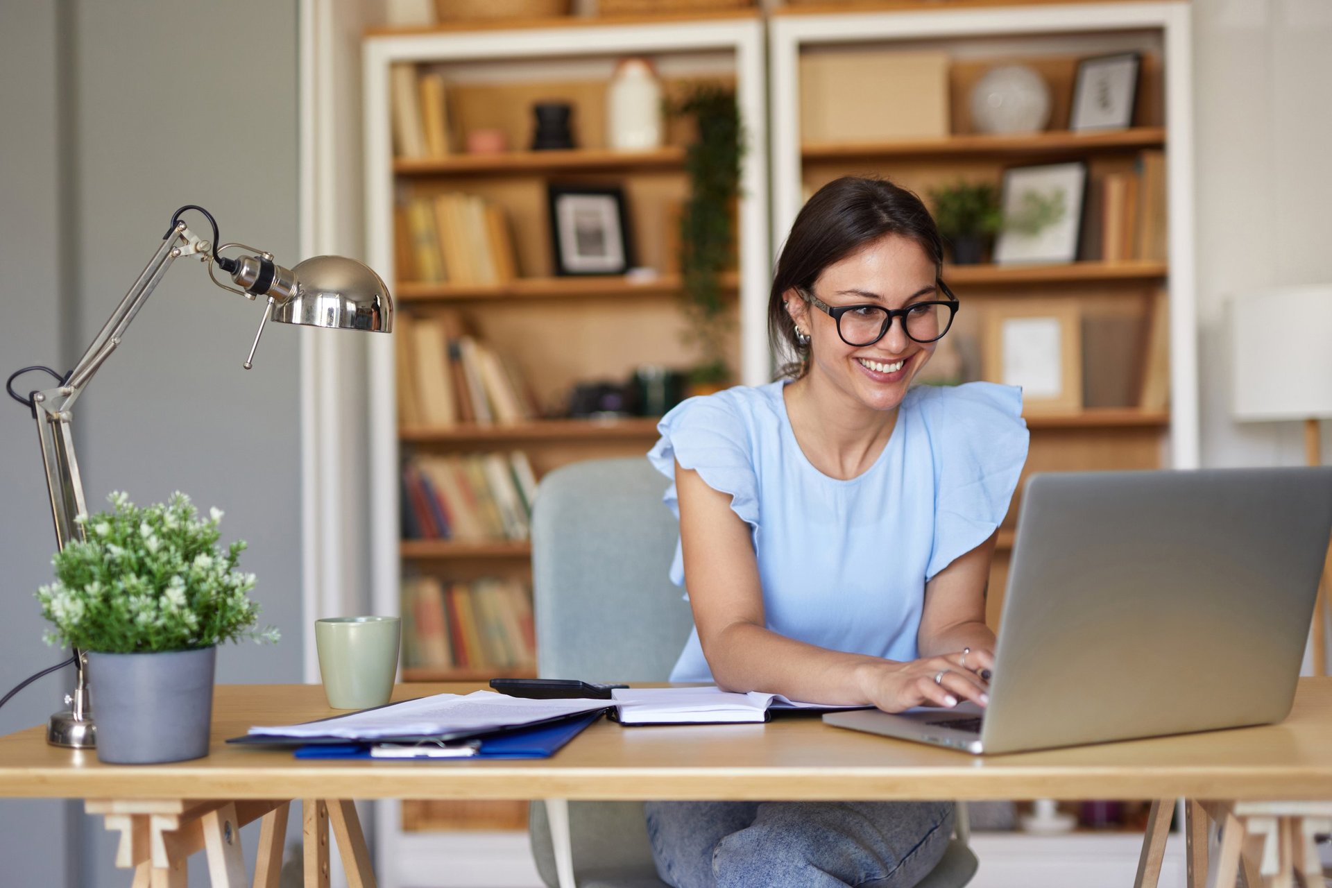 Smiling young woman working from home, typing on a laptop and looking at the screen.