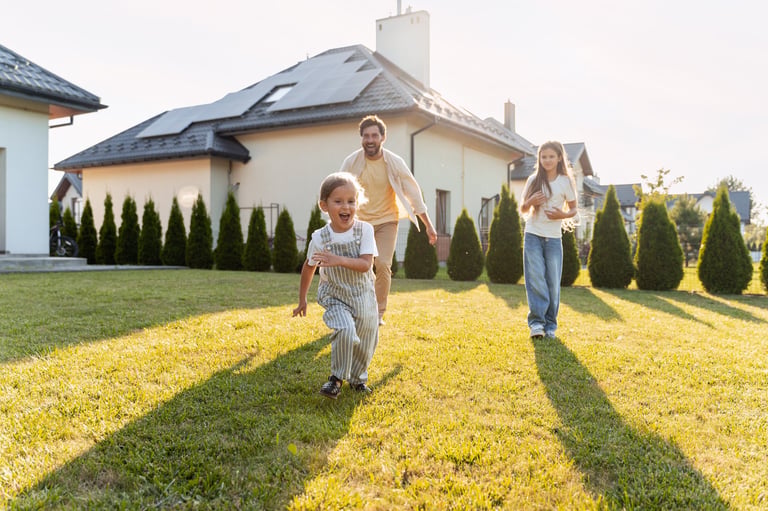 Father and children running on the lawn in front of their house with solar panels on the roof, enjoying a sunny day