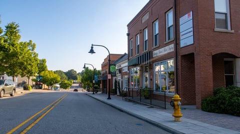 A quiet morning view of historic downtown with classic brick storefronts, tree-lined sidewalks