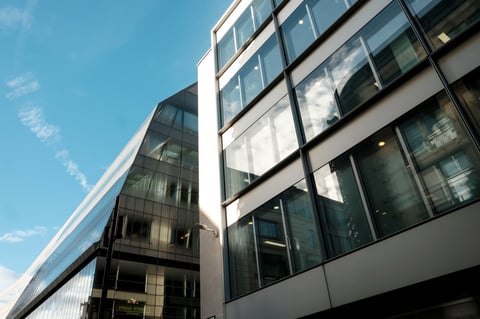 Contemporary commercial buildings featuring geometric glass facades and reflections of the blue sky, representing modern architecture, business, and urban development