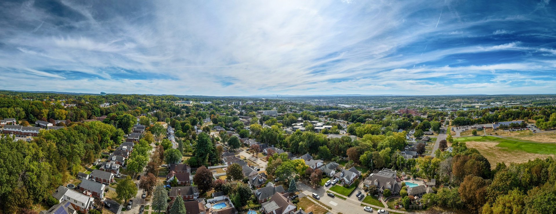A breathtaking sight of a spacious suburban area filled with houses and green trees. The sun shines brightly, illuminating the beauty of the landscape.