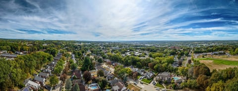 A breathtaking sight of a spacious suburban area filled with houses and green trees. The sun shines brightly, illuminating the beauty of the landscape.