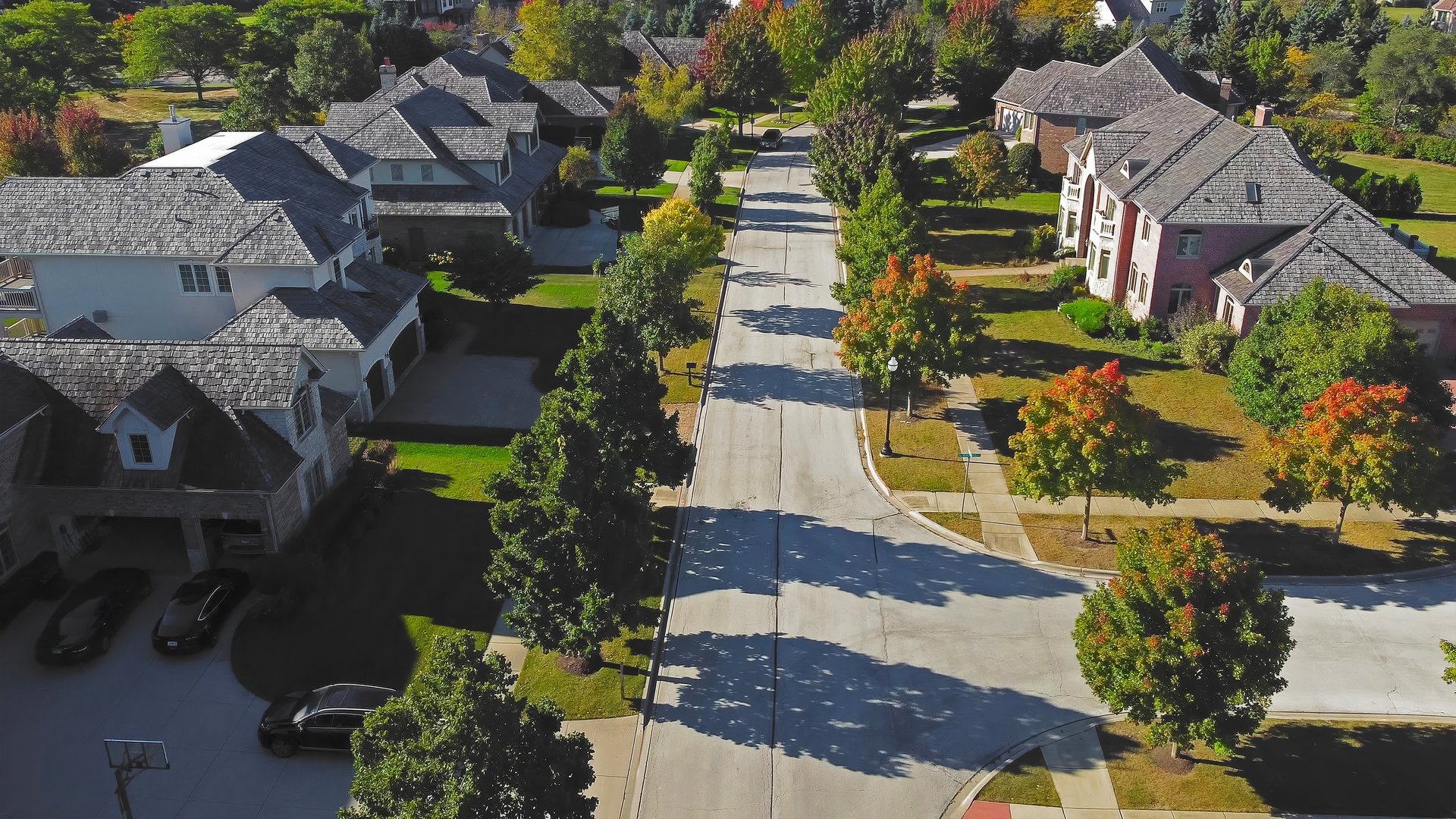 Aerial view of a peaceful residential street in Chicago with tree-lined sidewalks, well-maintained houses, and autumn-colored foliage casting long shadows under the bright sunlight.