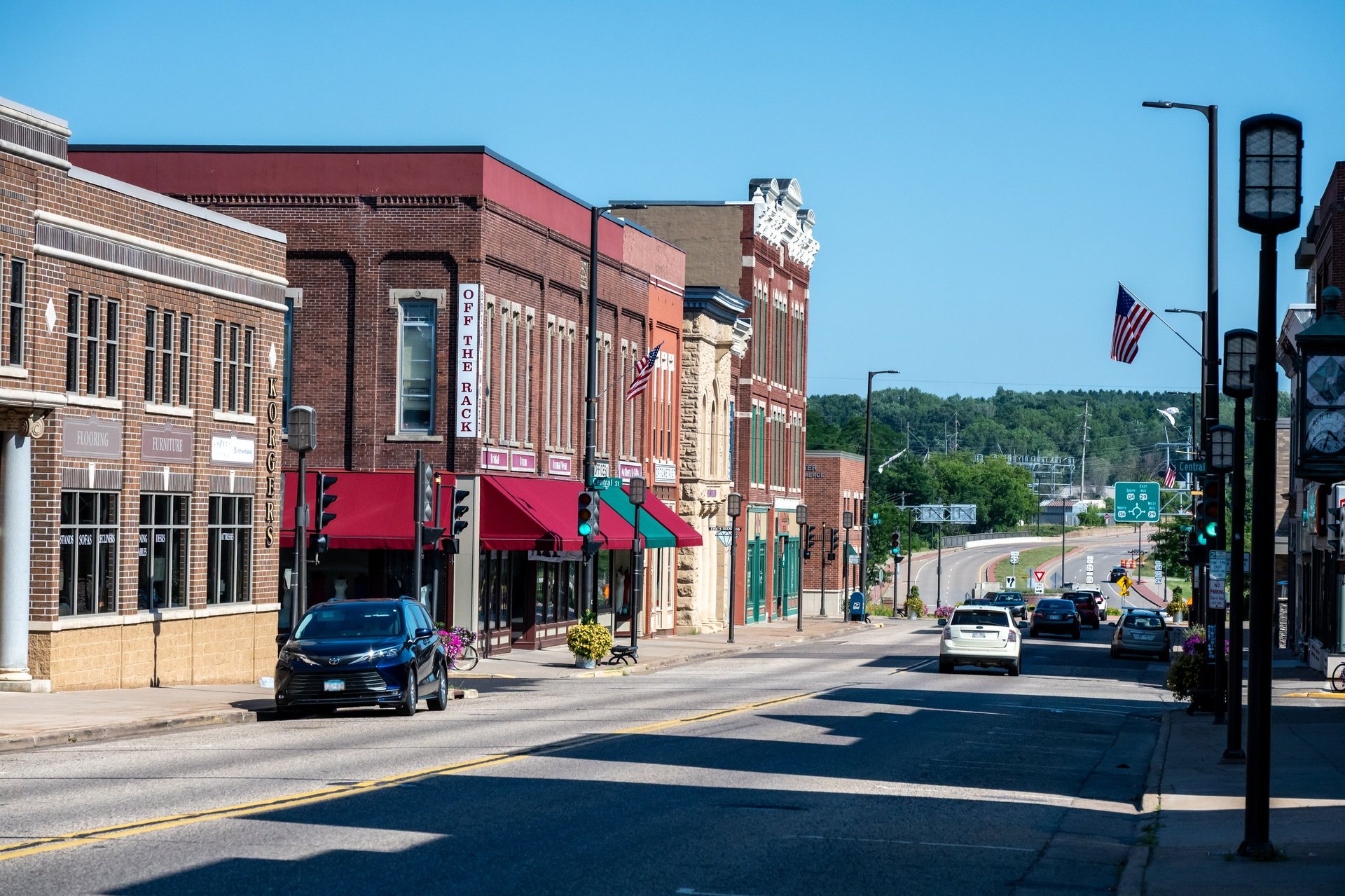 Chippewa Falls, WI, USA - Jul 12, 2026: Sunny historic downtown street with brick buildings, an American flag, and light traffic on a clear summer afternoon.