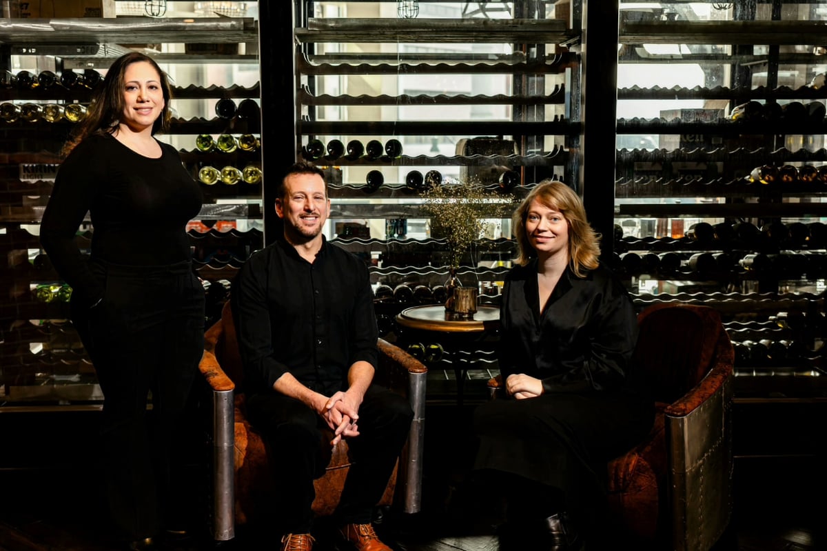 Three professionals posing in a wine cellar with illuminated racks of wine bottles in the background