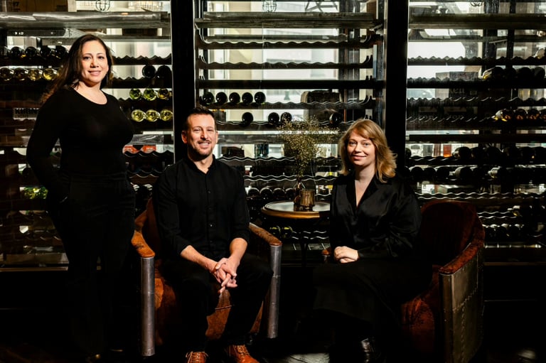 Three professionals posing in a wine cellar with illuminated racks of wine bottles in the background